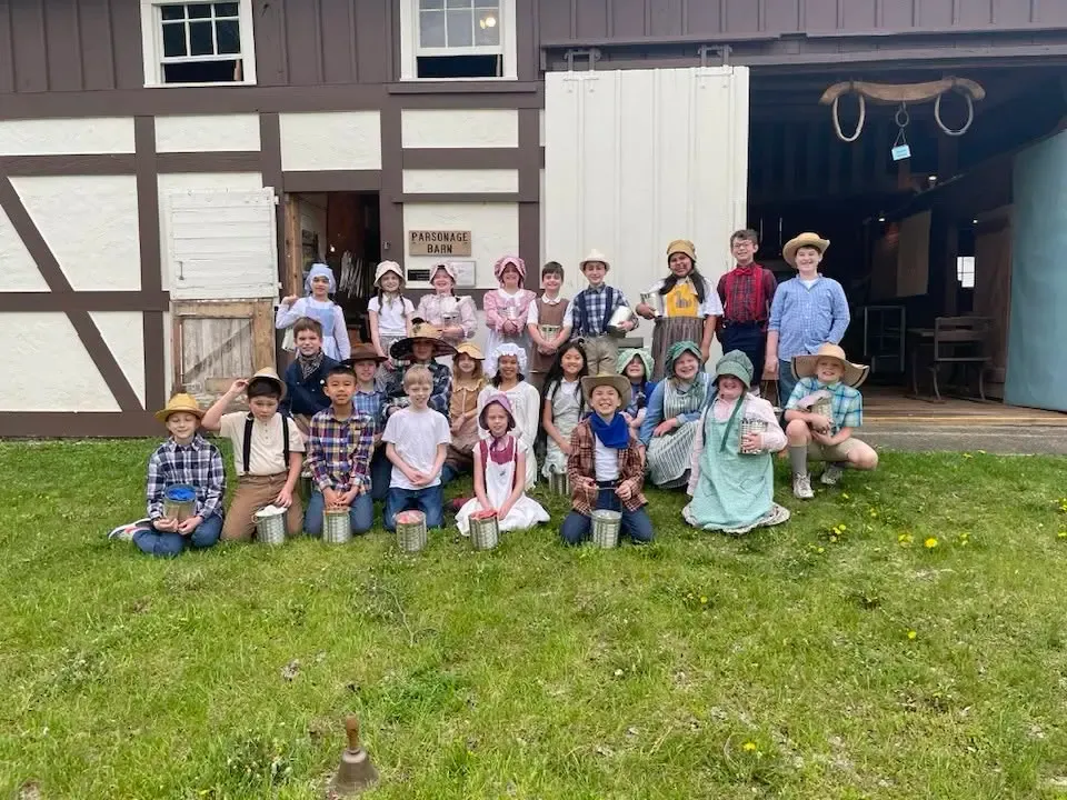 A school group in period dress gathered on the lawn in front of the half-timbered Parsonage Barn, its big doors open behind them