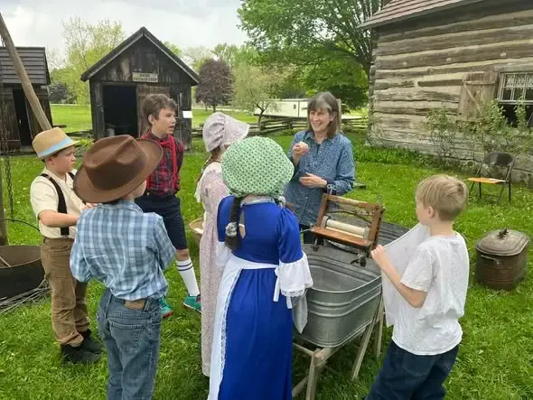 A volunteer showing schoolchildren how the hand-crank clothes wringer works over a washtub