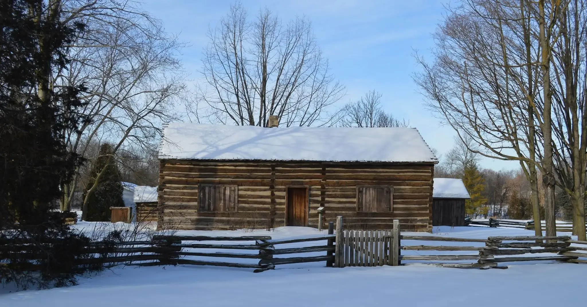 The historic log cabin in winter behind its split-rail fence, snow covering the ground
