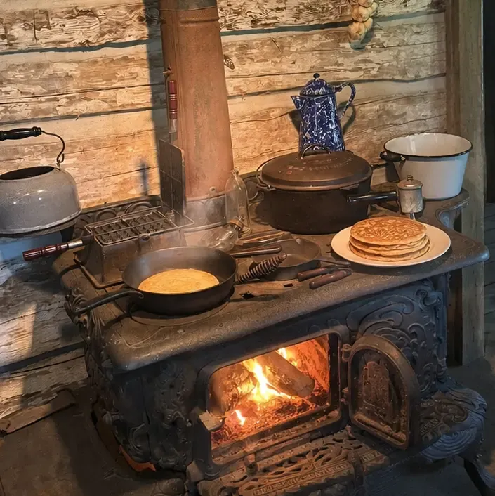 AI-rendered scene of pancakes on an antique wood-fired cook stove — a skillet on the griddle and a finished stack on a plate