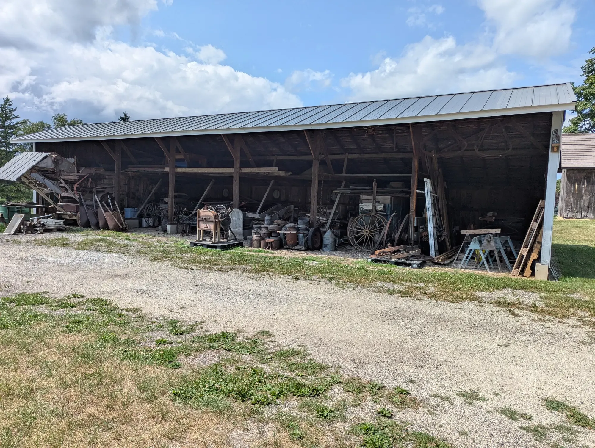 The long open-sided horse shed, its bays now filled with antique farm implements, wagon wheels, and milk cans