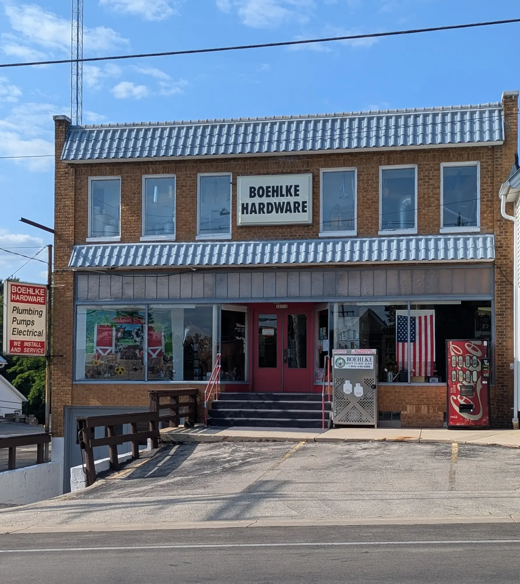 The 1929 brick Boehlke Hardware storefront — a model horse and farm mural in the display windows, red double doors up the front steps, and the plumbing-pumps-electrical sign at the corner