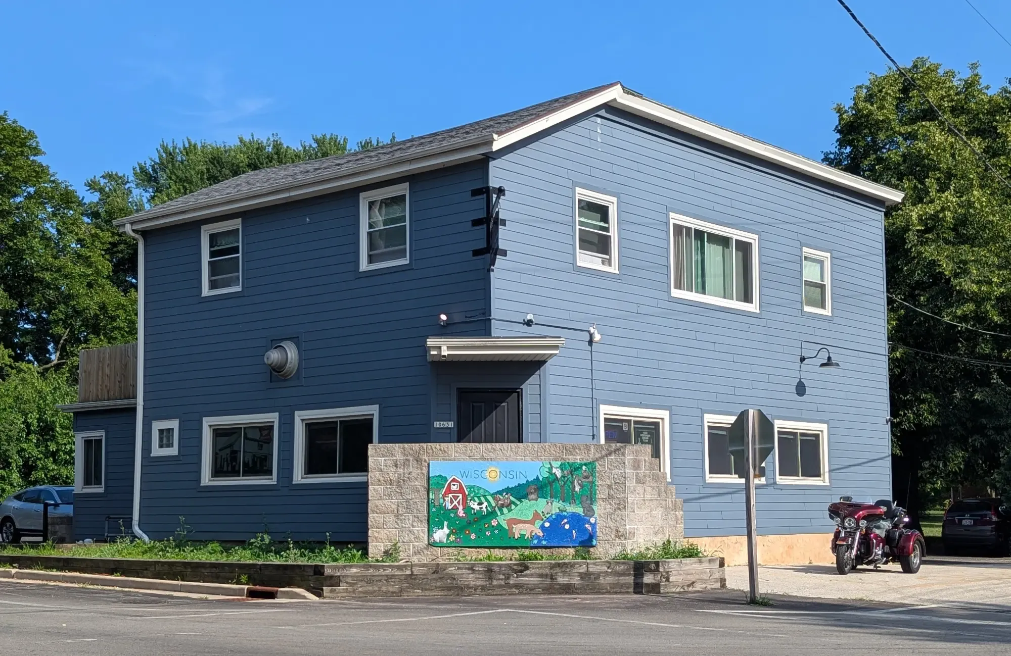 Korner-Q's blue two-story corner building at the crossroads, a colorful Wisconsin farm mural on the stone wall out front